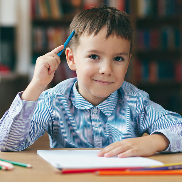 Cute  smiling boy doing homework,  coloring pages, writing and painting . Children paint. Kids draw. Preschooler with books in the library. Colorful pencils and paper on a desk. Creative boy.
