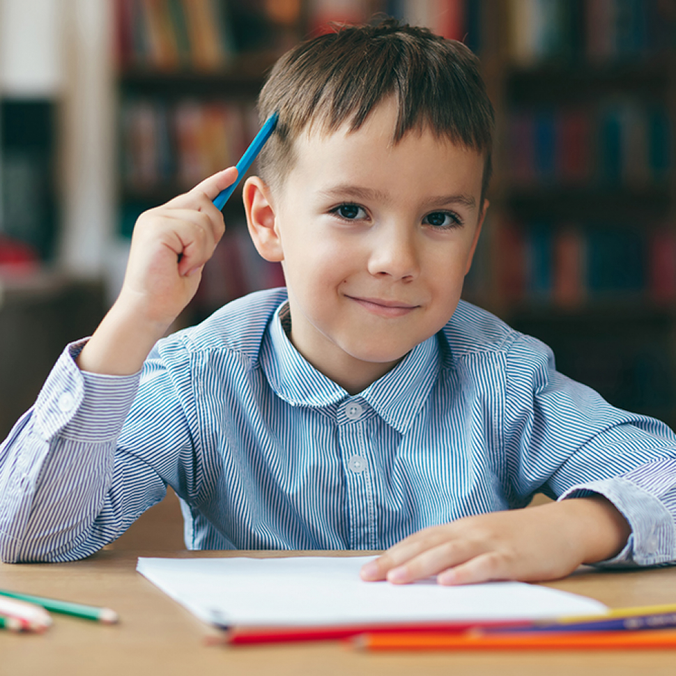 Cute  smiling boy doing homework,  coloring pages, writing and painting . Children paint. Kids draw. Preschooler with books in the library. Colorful pencils and paper on a desk. Creative boy.