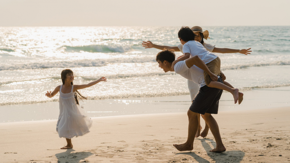 Asian young happy family enjoy vacation on beach in the evening. Dad, mom and kid relax playing together near sea when sunset while travel holiday. Lifestyle travel holiday vacation summer concept.