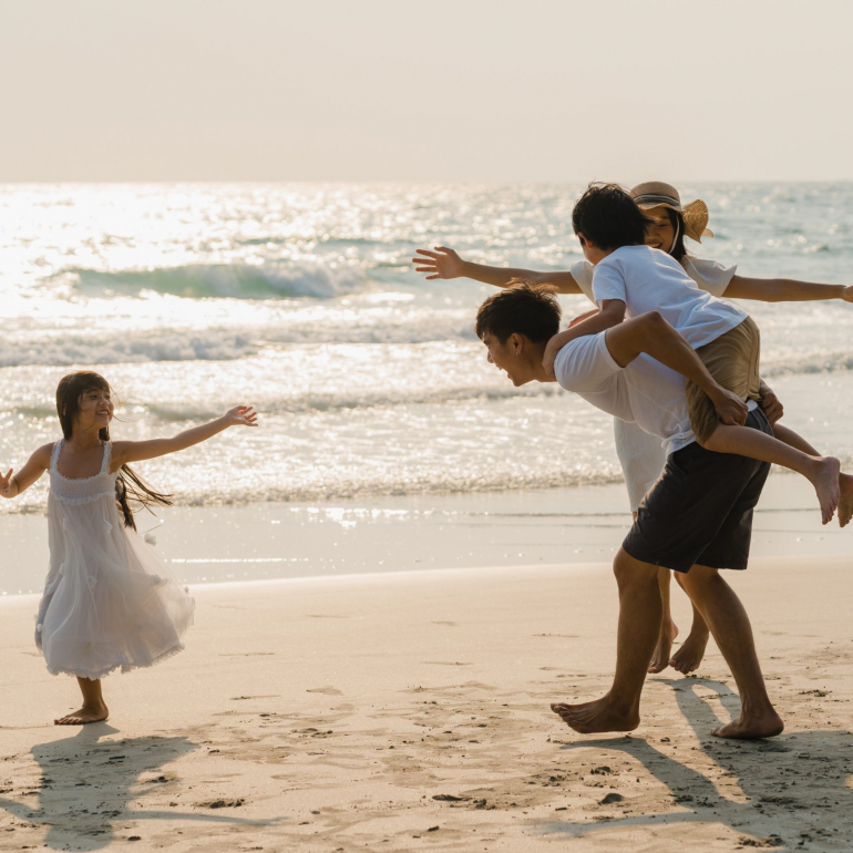 Asian young happy family enjoy vacation on beach in the evening. Dad, mom and kid relax playing together near sea when sunset while travel holiday. Lifestyle travel holiday vacation summer concept.