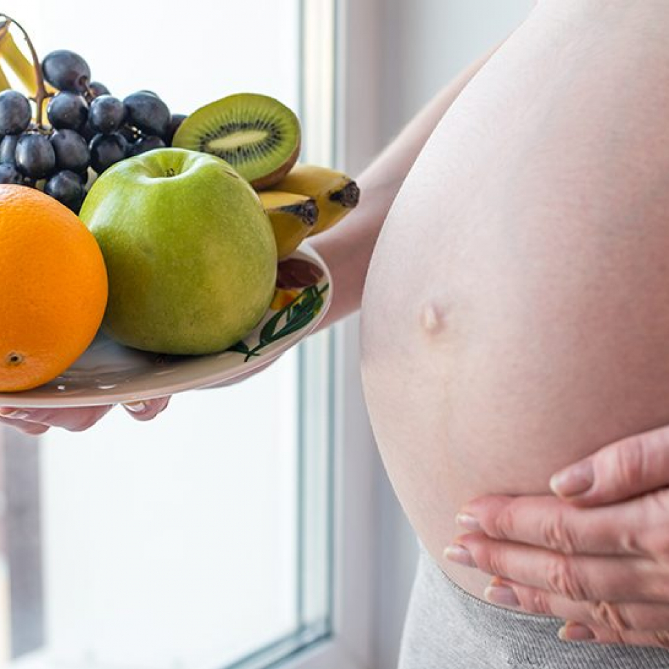 A pregnant woman with belly holding a plate with fruits in hand. The concept for weight control and healthy eating during pregnancy