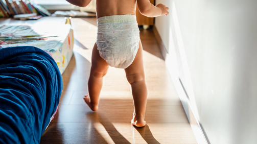 Baby in diapers learning to walk in her bedroom barefoot.