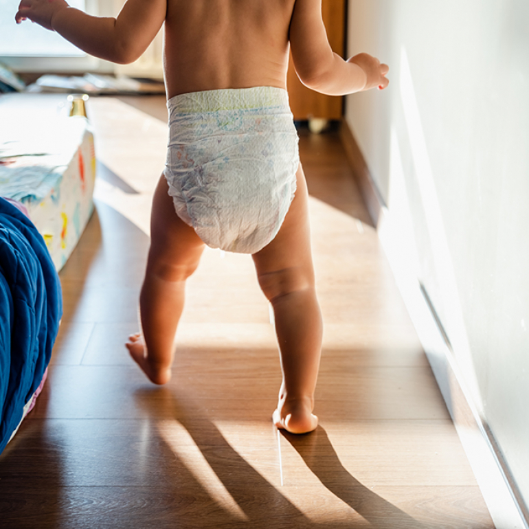 Baby in diapers learning to walk in her bedroom barefoot.