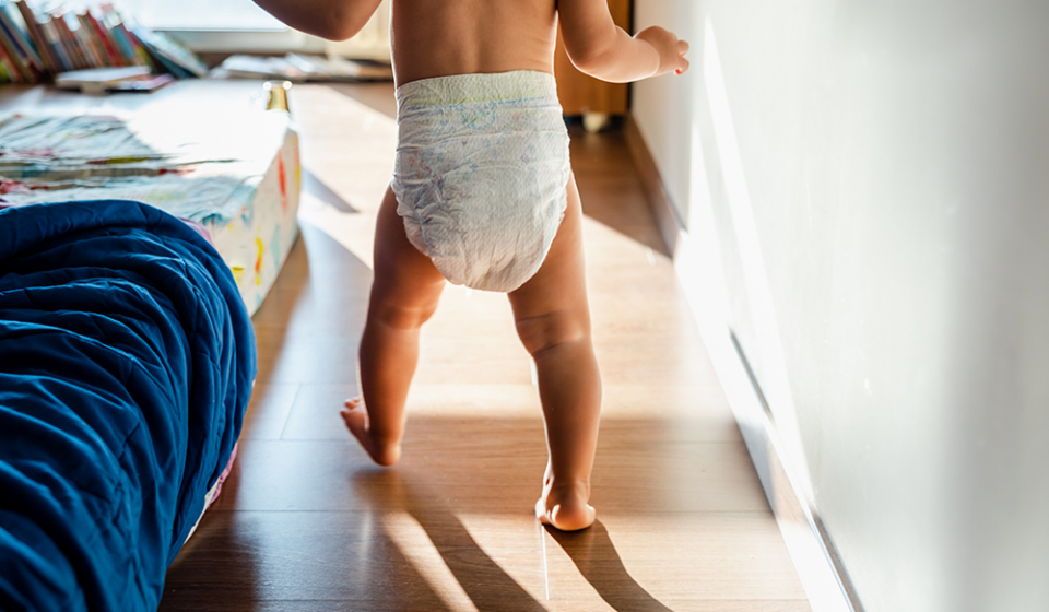 Baby in diapers learning to walk in her bedroom barefoot.