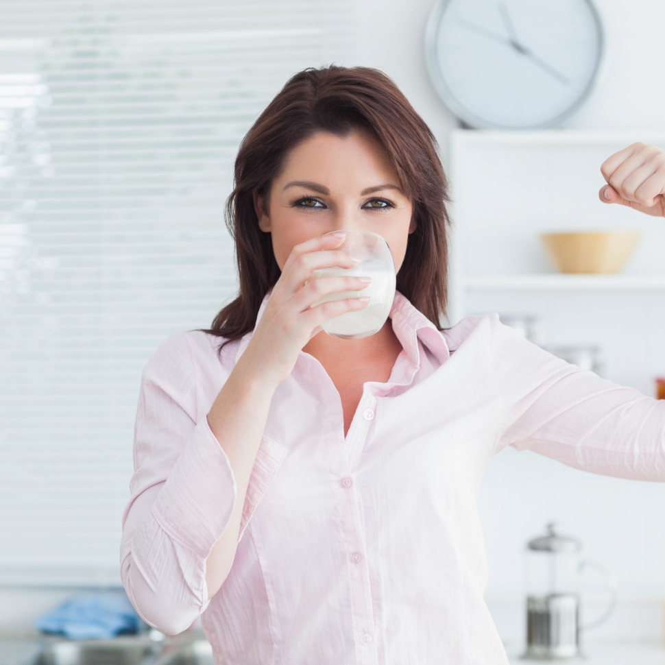 Portrait of young woman drinking milk and flexing muscles in the kitchen