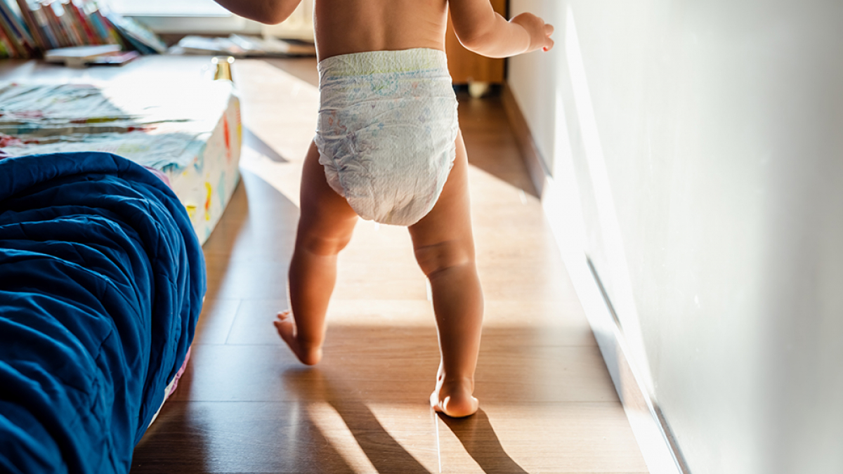 Baby in diapers learning to walk in her bedroom barefoot.